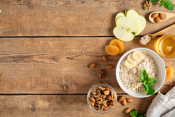 Ingredients for cooking healthy breakfast. Oatmeal, dried and fresh fruits, honey and nuts on a wooden table with copy space top view. Breakfast table concept
