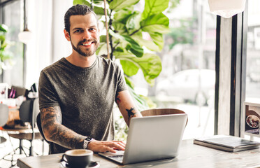 Handsome bearded hipster man use and looking at laptop computer with coffee at table in...