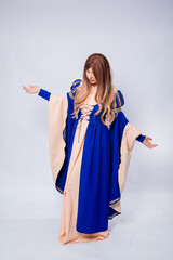 A full-length portrait of an attractive woman with long hair in a medieval, fantasy, blue and beige dress with long, large sleeves, posing isolated on a white background.