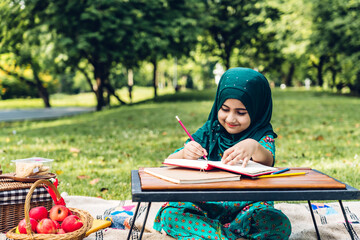 Portrait of happy little muslim girls child with hijab dress smiling and enjoy relax reading and write a book in summer park.Education concept