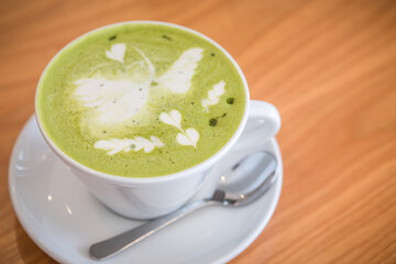 cup of hot matcha latte green tea with spoon on the wood table. Image has shallow depth of field.