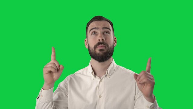 Happy young business man pointing finger up showing above then smile with thumbs up at camera. Portrait on green screen background.