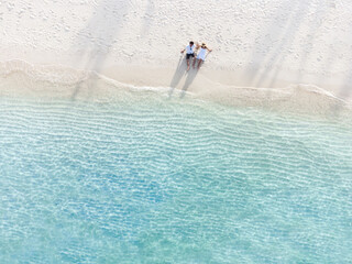 Young couple traveler sitting and relaxing at beautiful tropical white sand beach with wave foam...