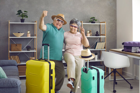 Let's rock this summer. Active senior couple having fun at home before going on holiday trip. Portrait of happy aged husband and wife with packed travel suitcases ready for cool vacation together
