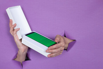 a new smartphone with a green screen in a package on a purple background, a girl holds in her hands, holes in the background