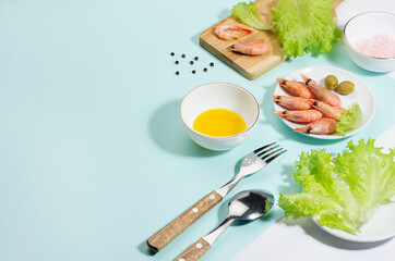 Fresh summer vitamin appetizer of green salad, shrimps, olive with shadow in sunlight on minty background, copy space, border. Seafood salad ingredients and cooking.