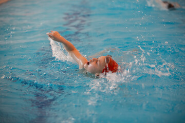 Boy in a swimming cap and swimming goggles in the pool. The child is engaged in the swimming section.