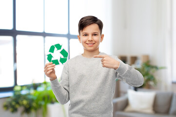 eco living, environment and sustainability concept - smiling boy showing green recycling sign over home room background
