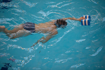 Boy in a swimming cap and swimming goggles in the pool. The child is engaged in the swimming...