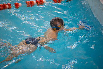 Boy in a swimming cap and swimming goggles in the pool. The child is engaged in the swimming...
