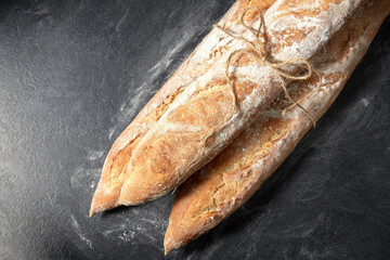 food, baking and cooking concept - pile of baguette bread loaves tied with rope on table over dark background