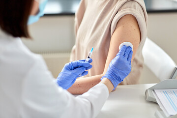 health, medicine and pandemic concept - close up of female doctor or nurse wearing protective medical gloves with syringe vaccinating patient at hospital