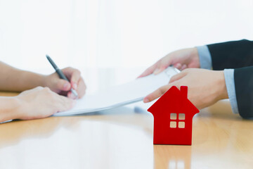 man signing a house insurance policy, the agent is holding the document. concept document sales loan and rental. focust red house on table