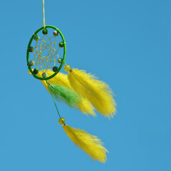 The yellow-green dreamcatcher is moving in the wind against the blue sky. Copyspace for the text.