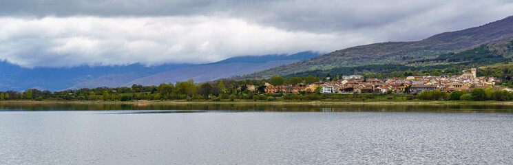 Fototapeta na wymiar panorama of a high mountain village on the shore of the lake with large clouds in dramatic sky.