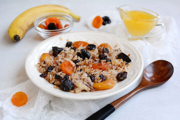 Close-up of rice porridge with dried apricots, prunes, bananas, honey, wood spoon on a light table on a white napkin
