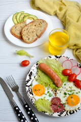Vertical view of plates with scrambled eggs, vegetables, bread and juice on a light wooden background