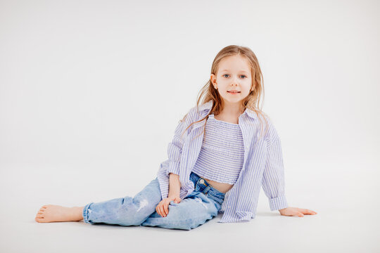 Little Girl With Long Hair In Jeans And Shirt Posing Against A White Background.