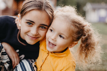 Obraz premium portrait of two cute little girls where a smaller curly girl hugs an older girl with freckles on her face