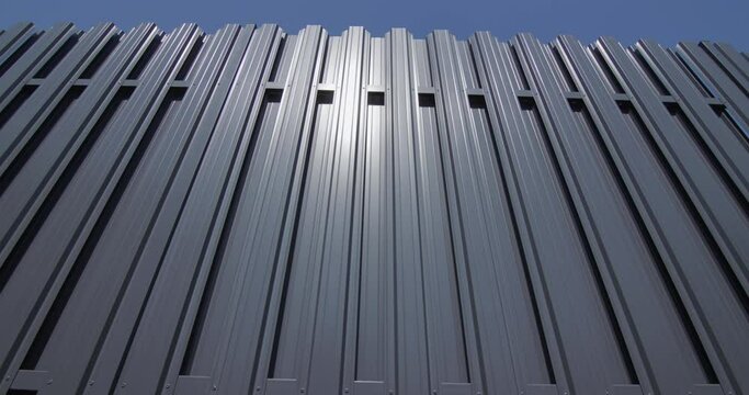 Slider shot: A fence made of grey metal stripes. Against the blue sky