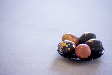 homemade colored golden Easter eggs on a plate against a gray linen tablecloth background with copy space. Spring, Easter decoration, religious fasting