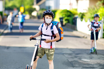 Little kid boy with glasses with medical mask on the way to school with scooter. Child with satchel. Schoolkid. Lockdown and quarantine time during corona virus covid pandemic disease. Open schools