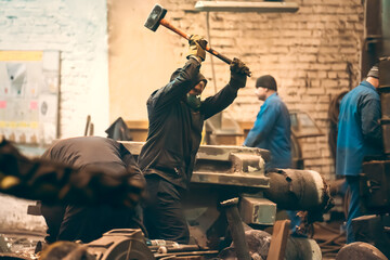 Worker swings a sledgehammer in a metal processing workshop.