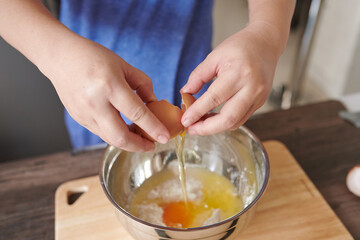 Fototapeta na wymiar Female hands crack egg into bowl for making dough 