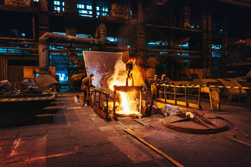 Foundry workshop interior, molten iron pouring from blast furnace into ladle container and workers...