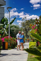 Fototapeta na wymiar Loving couple enjoying honeymoon in luxury hotel, walking through grounds with palm trees and beauty flowers