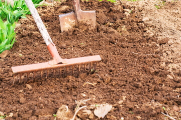 a dug up bed of earth a shovel is stuck in the ground in the foreground a rake in a blur