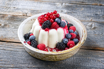 Modern style traditional blancmange almond pudding with wild berry coulis served as close-up in a...