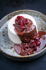 Modern style traditional blancmange almond pudding with cherry and chocolate cream and crumbles served as close-up in a Nordic design plate on a black board