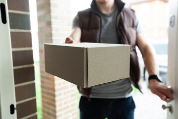 Deliveryman gives the carton box to the customer at the door of his house