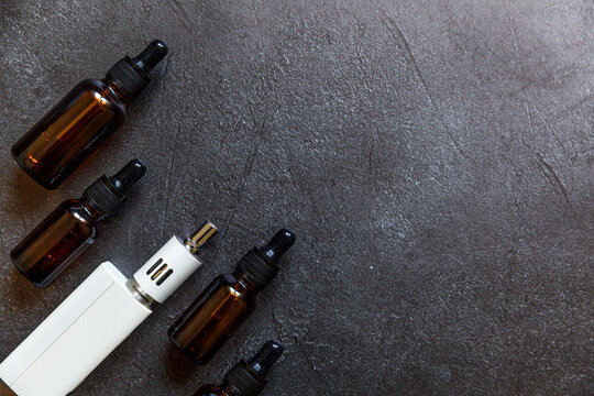 Vaping device e-cigarette electronic cigarette and liquid bottles on dark black stone shale background. Vape device for alternative smoking. Vaping shop concept. Gadget for vaper. Vaping accessories.