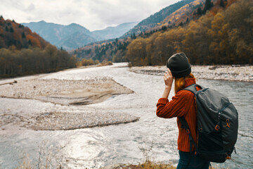 woman travel in the mountains on nature in autumn near the river and backpack hat sweater vacation