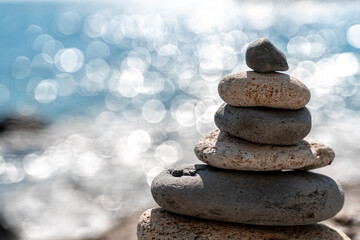 Tower of stones. Balanced pebble pyramid on the beach on a sunny day. Blue sea on the background. Selective focus, bokeh. Zen stones on the sea beach, meditation, spa, harmony, tranquility, balance