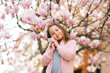 Fototapeta premium Beautiful smiling little girl in the spring garden near blooming magnolia tree