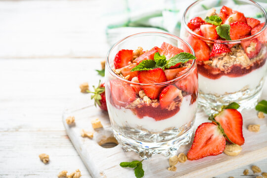 Greek yogurt parfait with strawberry at white table.