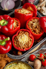 Red bell stuffed paprika peppers in iron cooking pot with various ingredients on side