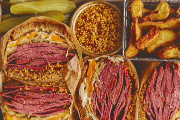 Enormous sandwiches with pastrami beef in wooden box. Served with baked potatoes, pickles