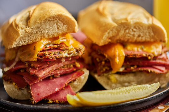 Delicious pastrami meat sandwiches served with glass of beer, pickles, potato chips and sides.