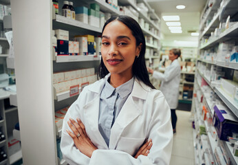 Young pharmacist with crossed arms looking at camera in drugstore