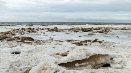 the river estuary to the sea, winter day, ice shapes on the sea shore, cloudy weather, blurred sky