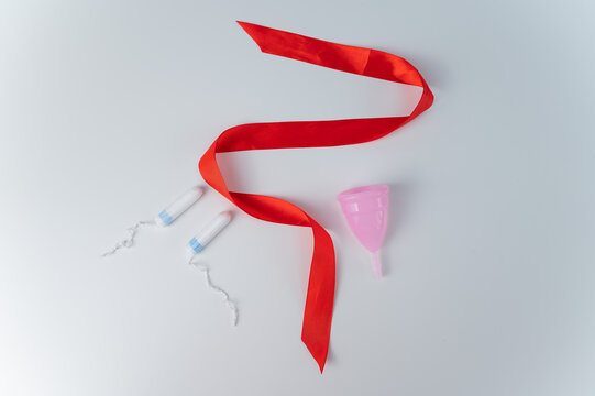 Tampon, pink menstrual cup and red satin ribbon on a white background. Means of intimate hygiene of a woman during mentruation