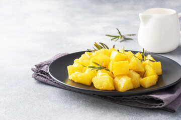 Delicious baked potatoes with spices cheese and rosemary on a black ceramic plate, a gray concrete background, copy space.