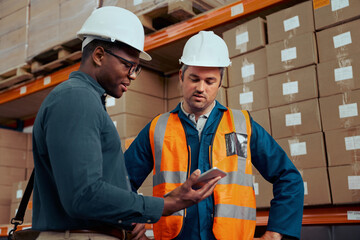 Multiracial factory engineers looking at digital tablet with stacked boxes at background