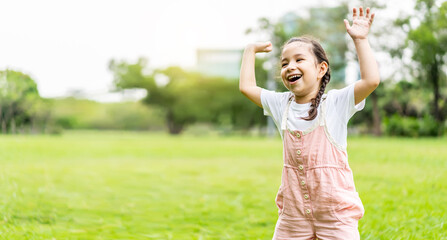 Portrait of happy pretty child girl smiling and raises her hand while standing in the park, ​Positive female kid enjoying warm day in fall park