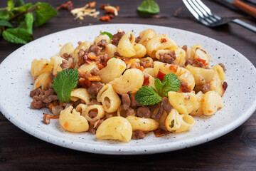 Stewed pasta with minced beef and vegetables, macaroni in Navy style on a plate. Dark wooden background.