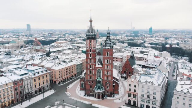 Drone footage of St Mary's Basilica (Mariacki Church) in the Main Market Square in the Old Town of Krakow, Poland. Historic buildings. Footage is made during the daytime. Clear white sky in he